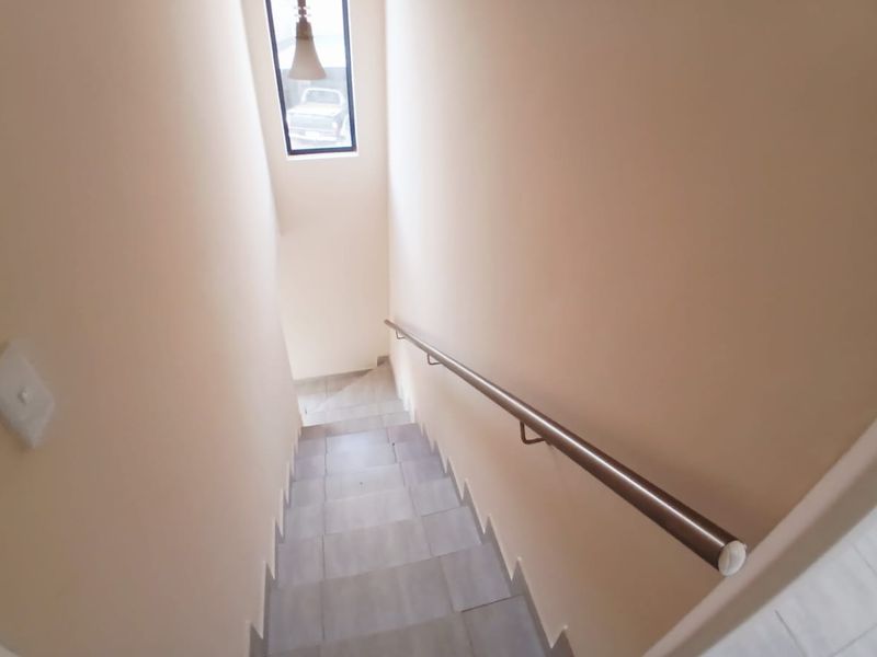 A clean, minimalist staircase featuring tiled steps, a modern metal handrail, and a vertical window providing natural light.