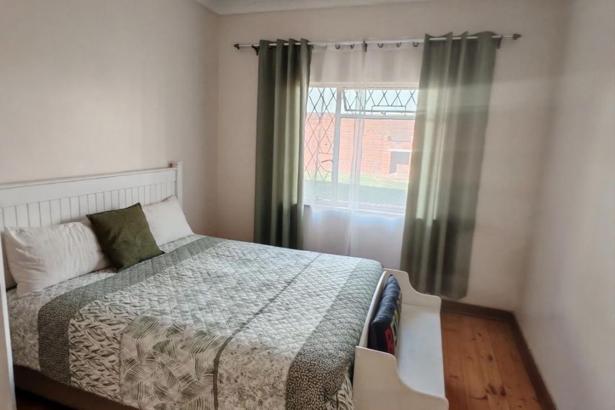 A cozy bedroom featuring warm timber flooring, neutral wall finishes, and a window fitted with security bars.
