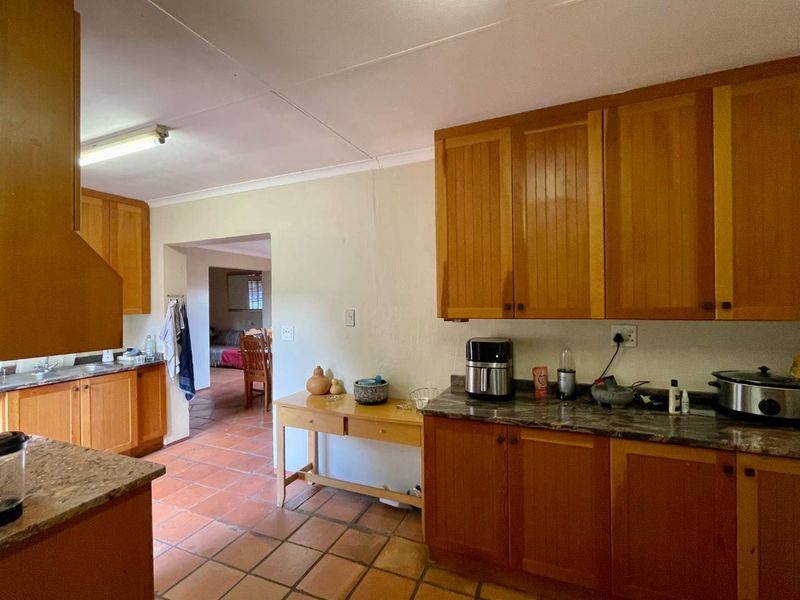 A functional kitchen featuring wooden cabinetry, laminate countertops, and terracotta floor tiles, with an open layout leading into the adjacent living area.