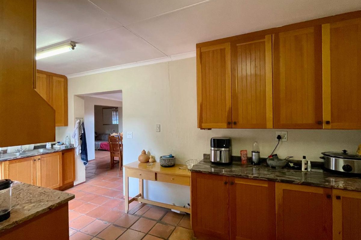 A functional kitchen featuring wooden cabinetry, laminate countertops, and terracotta floor tiles, with an open layout leading into the adjacent living area.