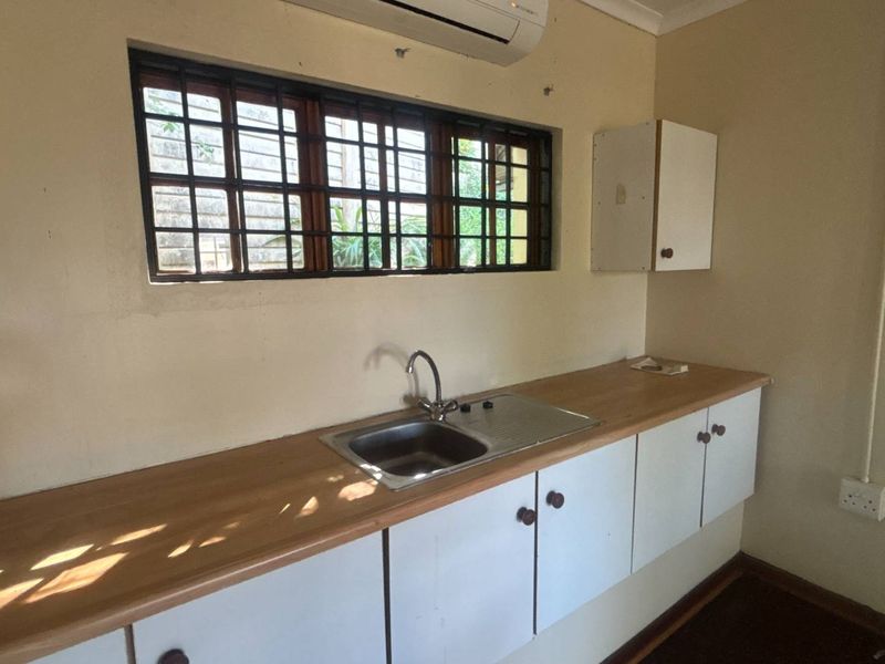 A functional kitchen area featuring a stainless steel sink, laminate countertop, built-in cabinetry, and a wall-mounted air conditioning unit.
