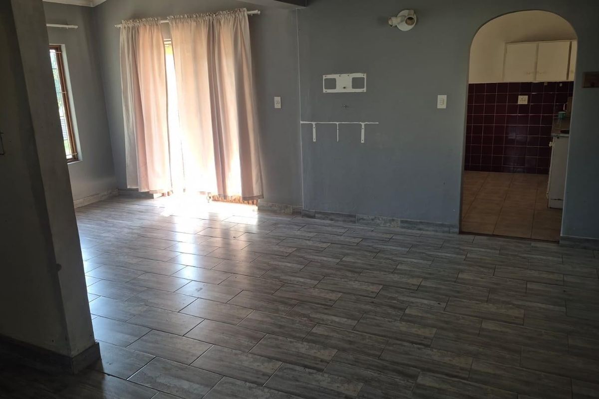 An empty living room featuring wood-look tiled flooring, an arched doorway leading to the kitchen, and a sliding door providing access to the exterior.