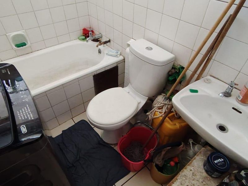 Compact bathroom featuring a bathtub, toilet, and washbasin with white wall tiling. The space requires cosmetic updates to improve its overall condition.