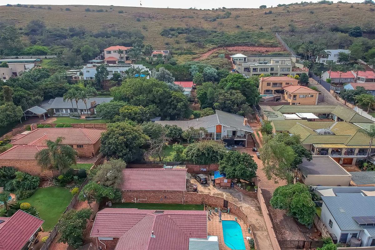 An aerial view of a residential neighborhood featuring various houses with tiled roofs, swimming pools, and established garden landscaping.