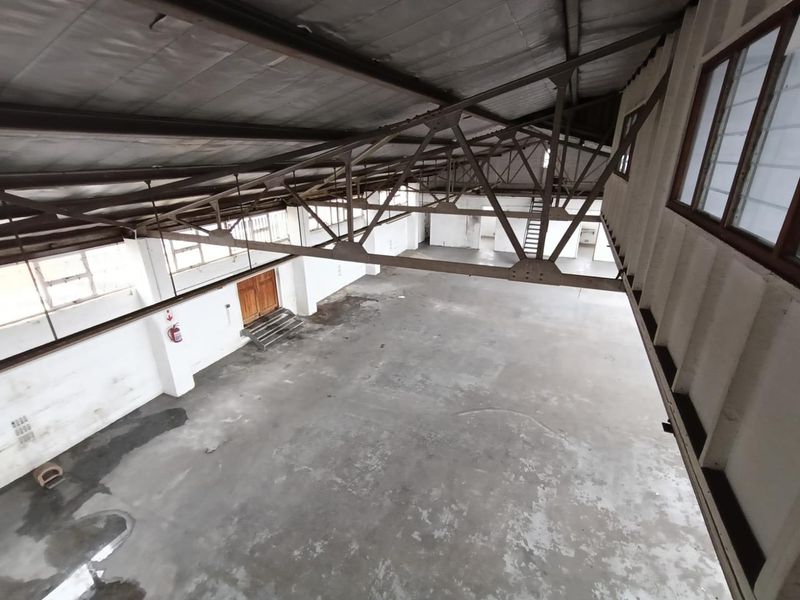 Spacious industrial warehouse area featuring high ceilings with exposed steel trusses, concrete flooring, and a mezzanine level, suitable for various commercial or storage uses.