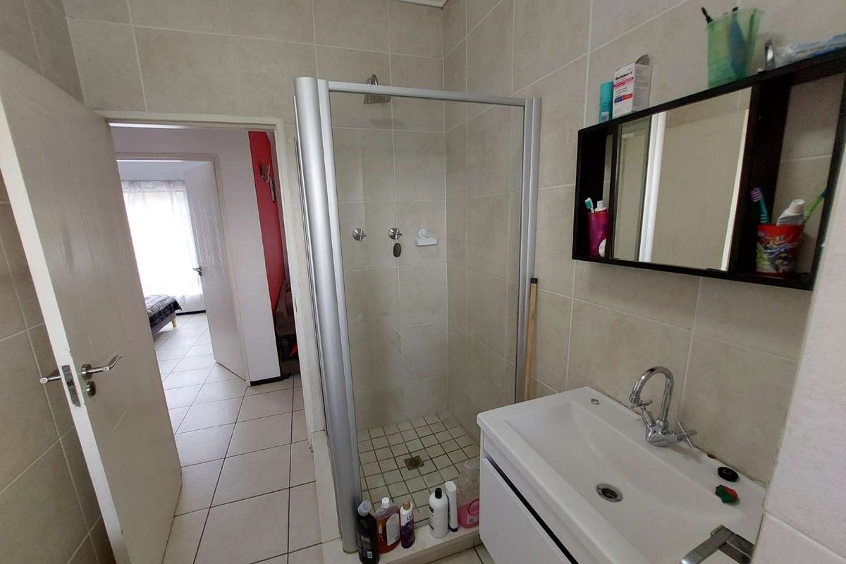 A functional bathroom featuring a glass-enclosed shower, a modern vanity with a basin, and neutral wall and floor tiling.