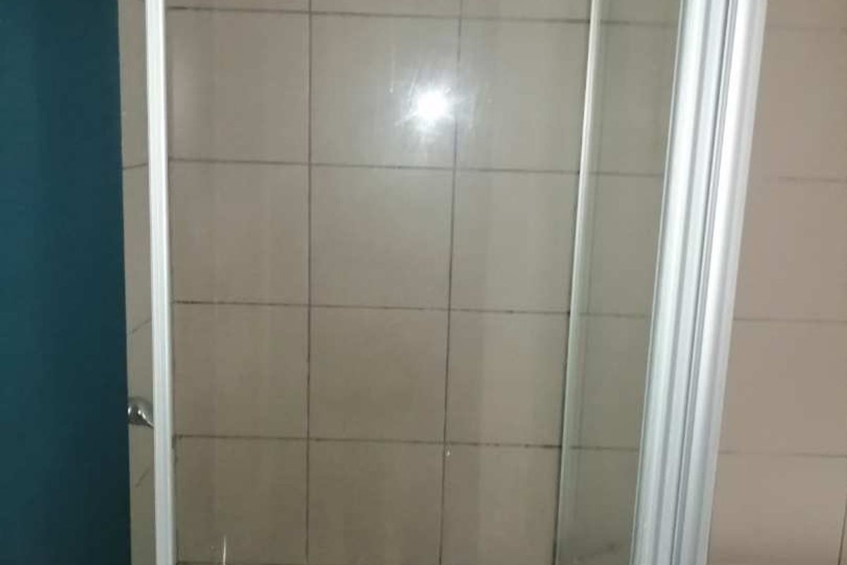 A functional bathroom featuring a glass-enclosed shower with tiled walls and a separate bathtub, presenting a clean but dated aesthetic.