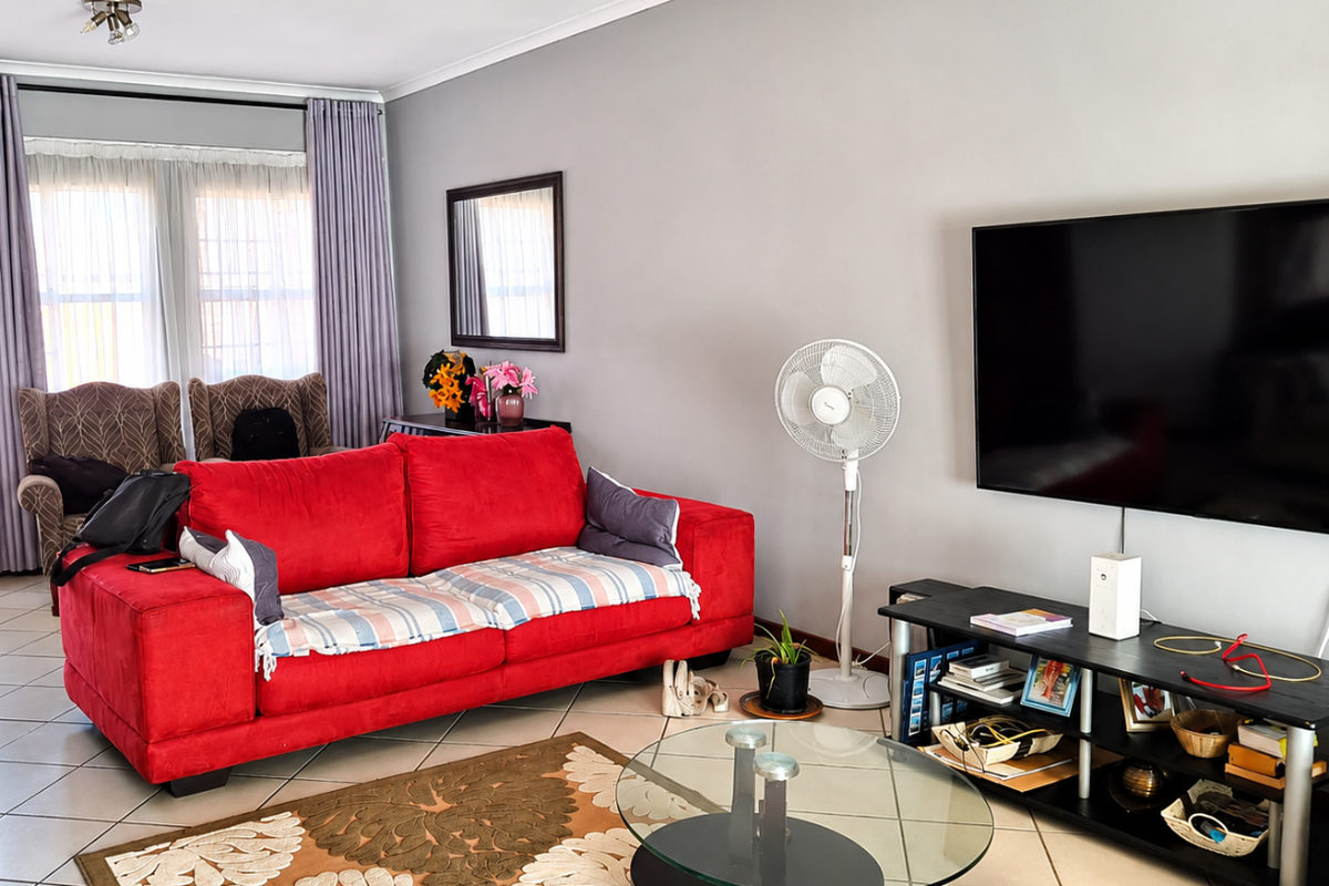 A spacious living room featuring tiled flooring, large windows with curtain tracks, and a wall-mounted television setup.