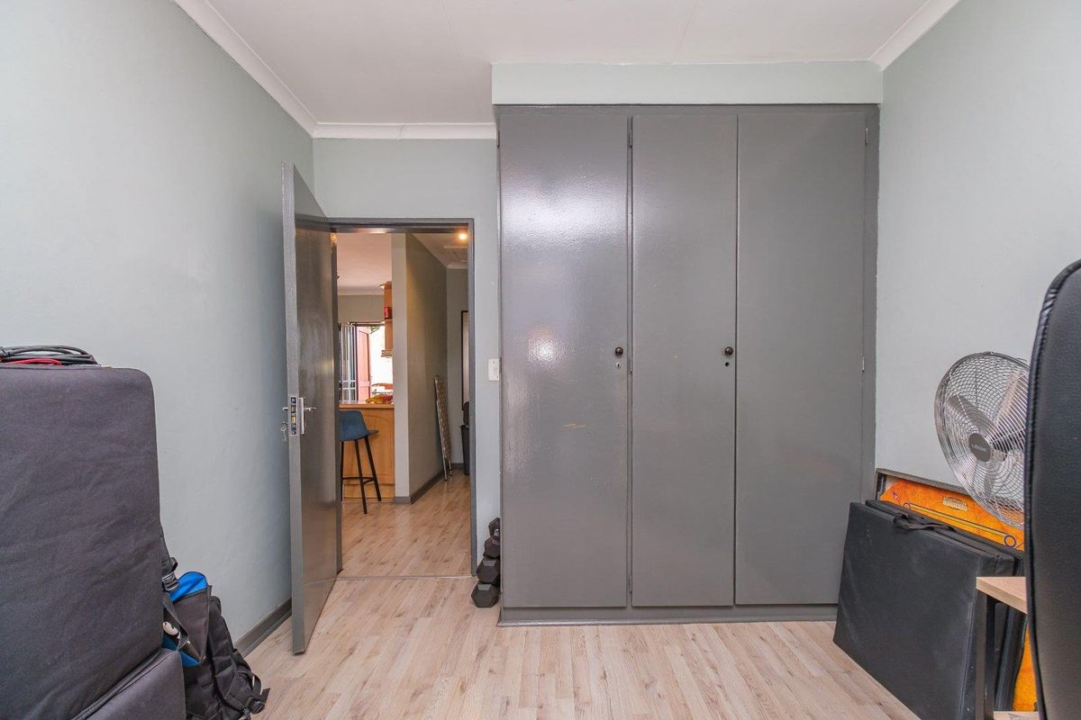 A bedroom featuring light wood-look flooring and built-in grey cabinetry, with a doorway leading to an adjacent living area.