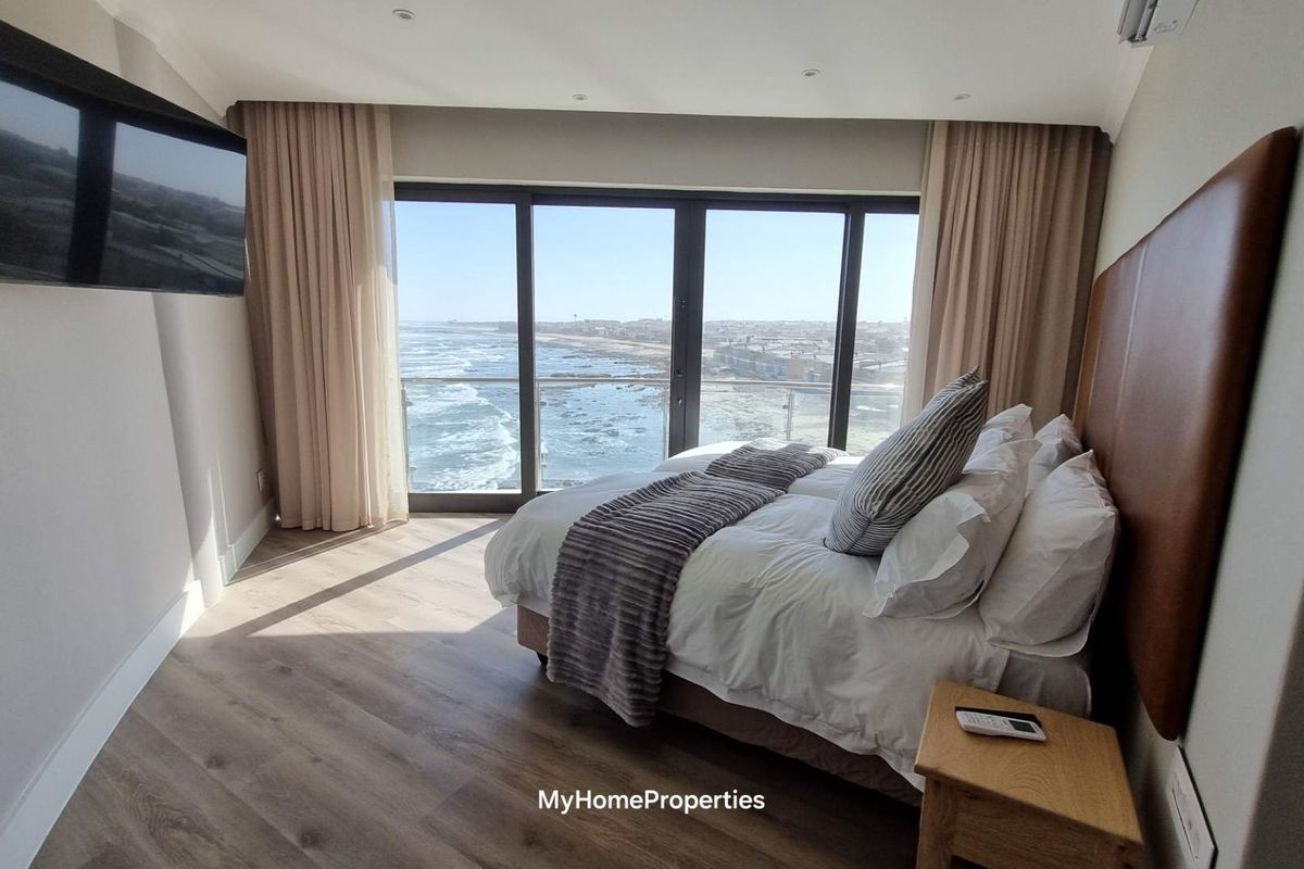 Modern bedroom featuring laminate flooring, recessed lighting, and large sliding glass doors offering expansive ocean views.