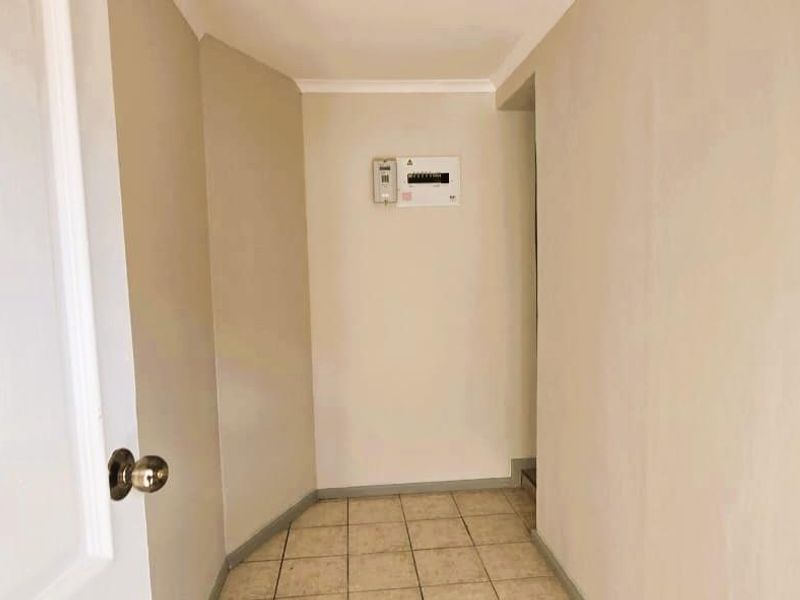 A clean, neutral-toned hallway featuring tiled flooring and a wall-mounted electrical distribution board.