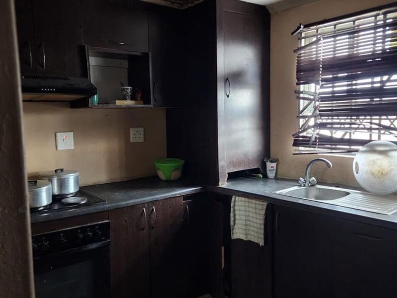A compact kitchen featuring dark cabinetry, built-in appliances, and tiled flooring, currently requiring ceiling repairs and general refurbishment.