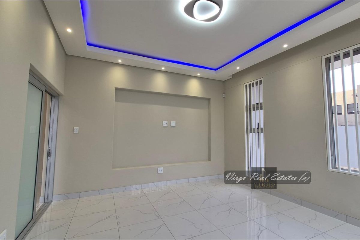 A modern, empty living room featuring polished porcelain floor tiles, a recessed television niche, and a contemporary ceiling design with integrated LED accent lighting.