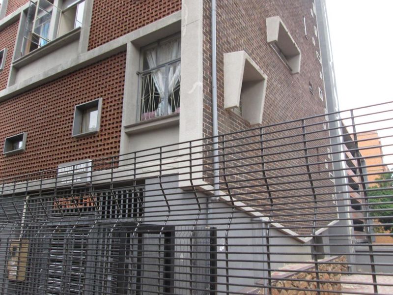 Exterior view of an apartment building facade featuring brickwork, concrete architectural details, and perimeter security fencing.