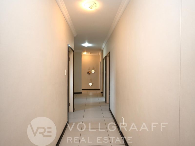 A clean, neutral hallway featuring tiled flooring and simple ceiling lighting, providing access to multiple rooms within the home.