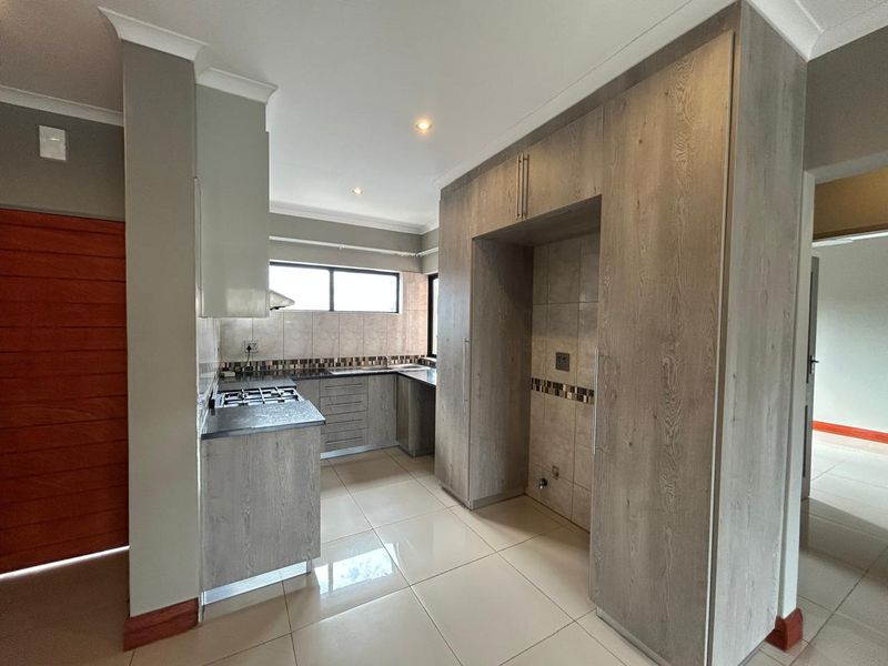Modern kitchen featuring light wood-grain cabinetry, gas hob, extractor fan, tiled backsplash, and neutral floor tiles in an open-plan layout.