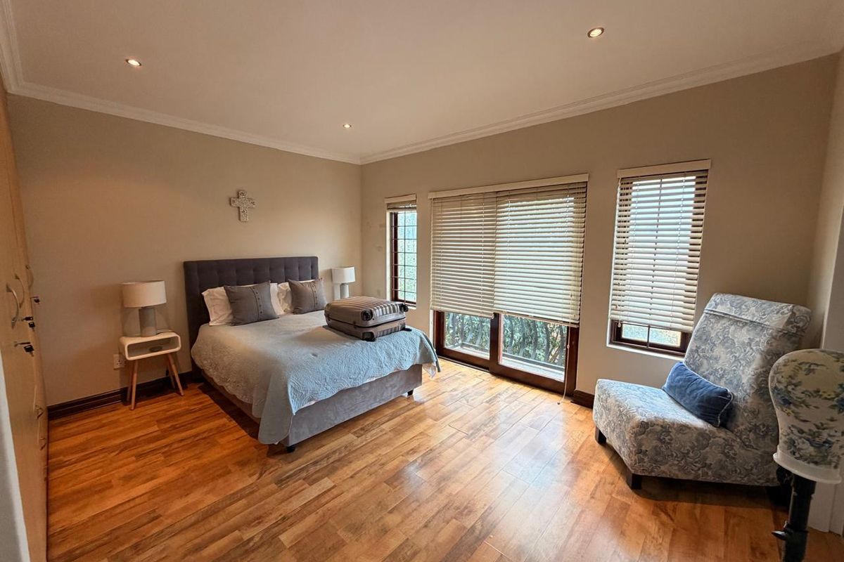 Spacious bedroom featuring warm hardwood flooring, built-in cupboards, and large sliding doors with venetian blinds allowing for ample natural light.