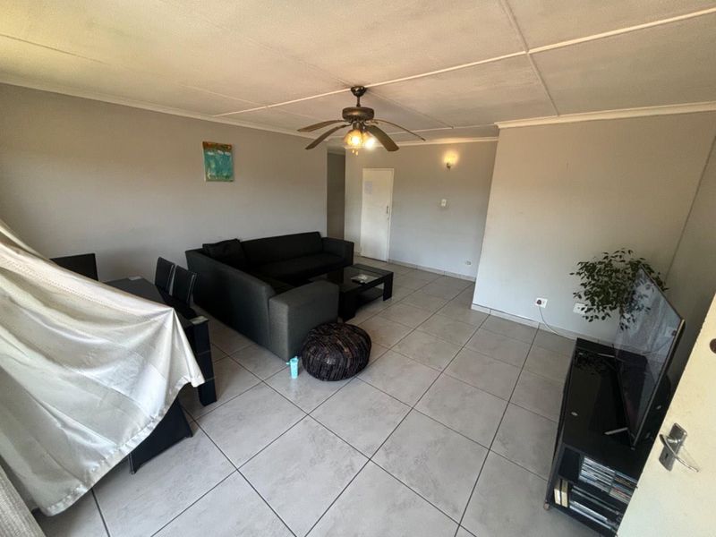 A spacious living area featuring neutral tiled flooring, a ceiling fan, and coved ceiling details, offering a functional layout for comfortable daily living.