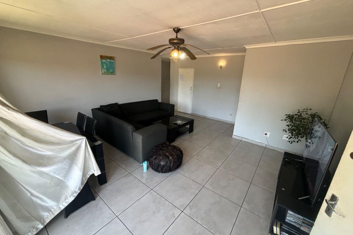 A spacious living area featuring neutral tiled flooring, a ceiling fan, and coved ceiling details, offering a functional layout for comfortable daily living.