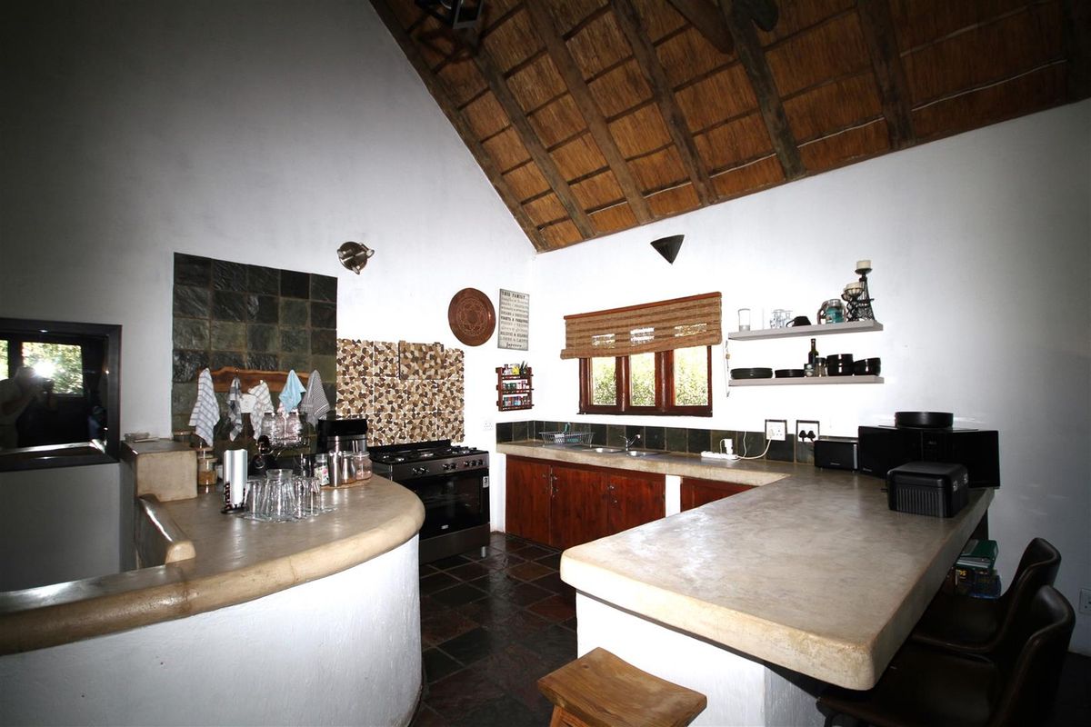 Rustic kitchen featuring a high thatched ceiling, built-in concrete countertops, dark cabinetry, and slate tile flooring in an open-plan layout.