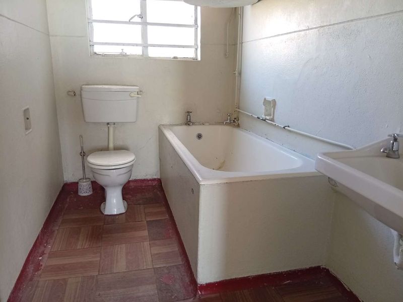 A dated bathroom featuring a standard bathtub, toilet, and washbasin, requiring renovation to update the finishes and fixtures.