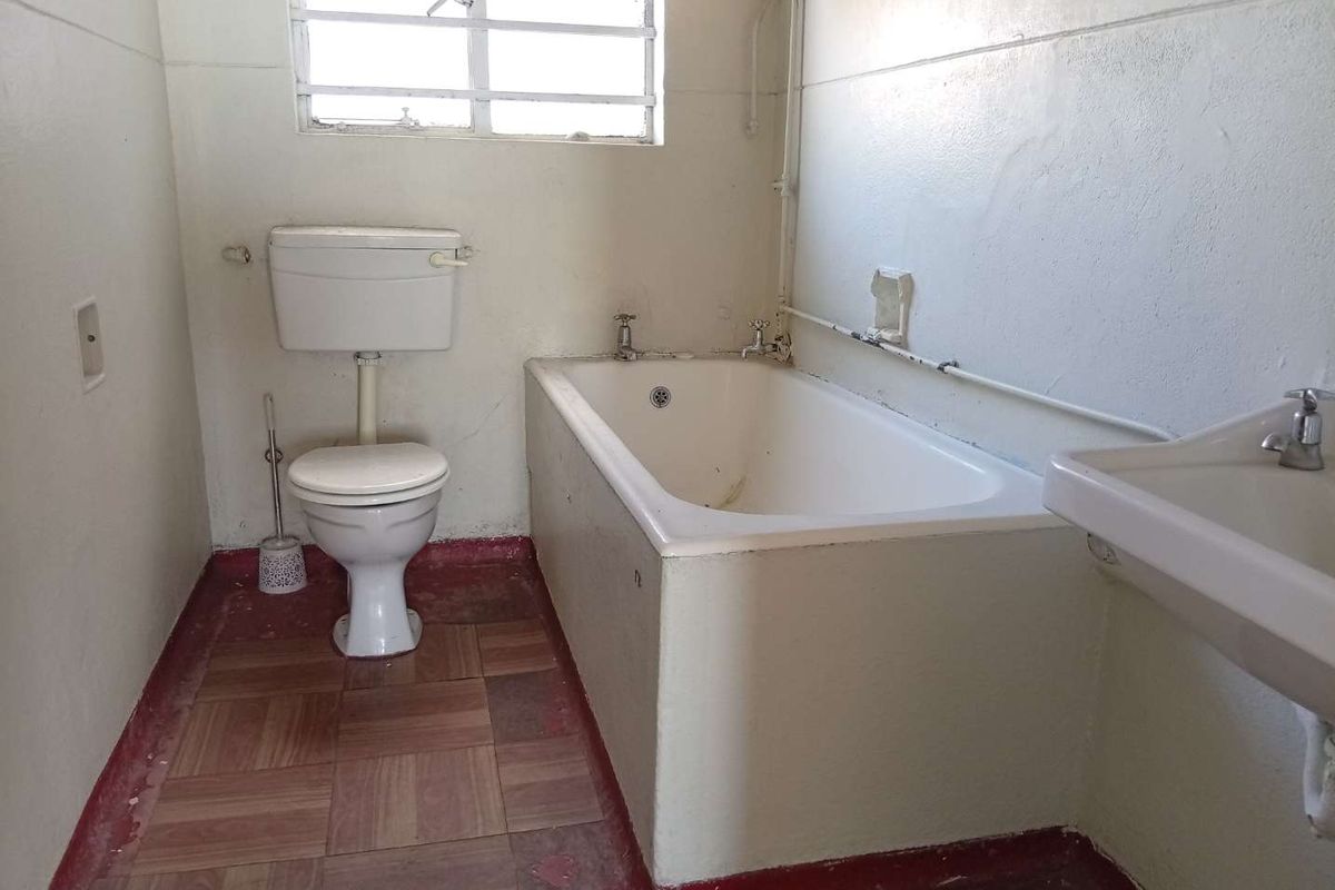 A dated bathroom featuring a standard bathtub, toilet, and washbasin, requiring renovation to update the finishes and fixtures.