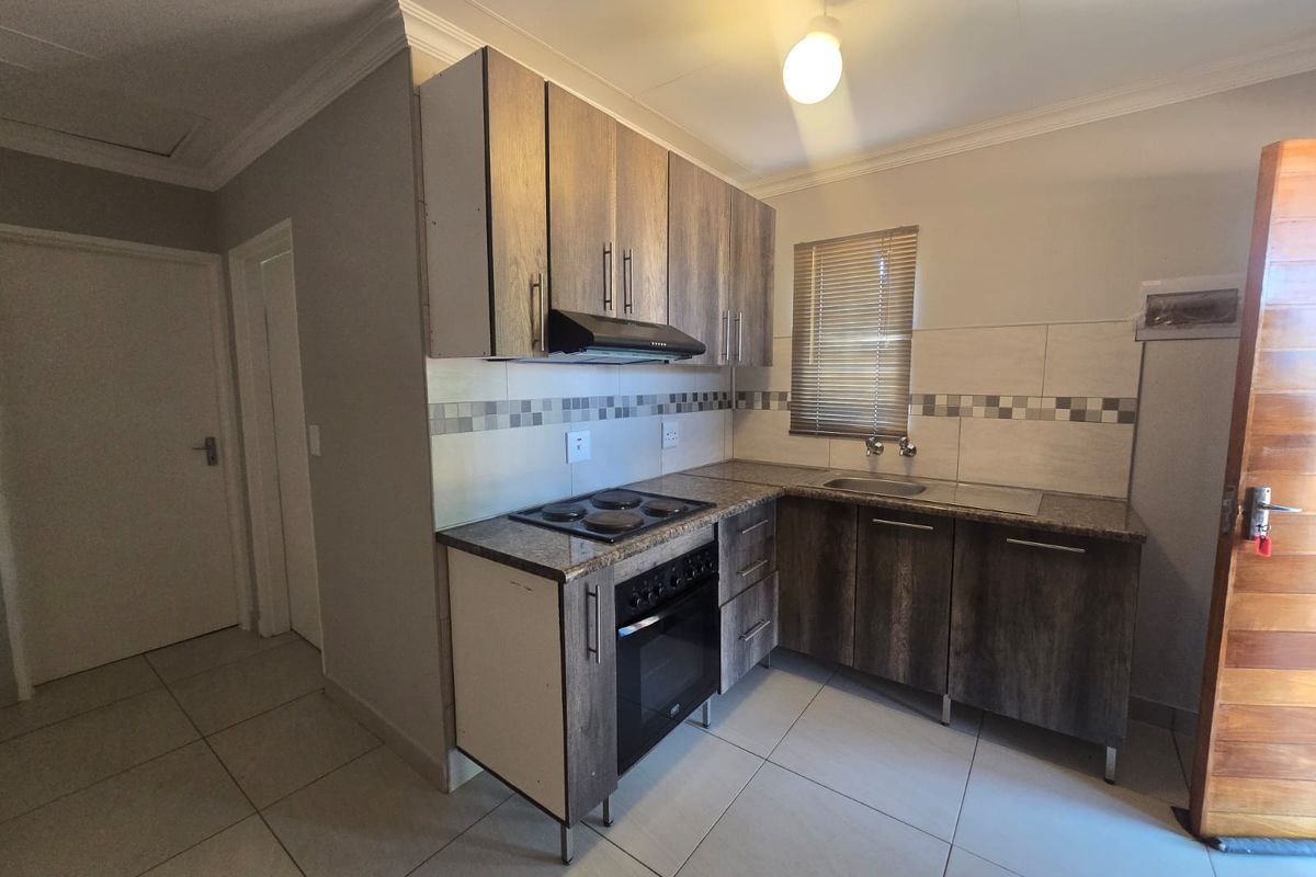 Compact kitchen featuring wood-look cabinetry, built-in electric oven and hob, tiled splashback, and neutral floor tiles.