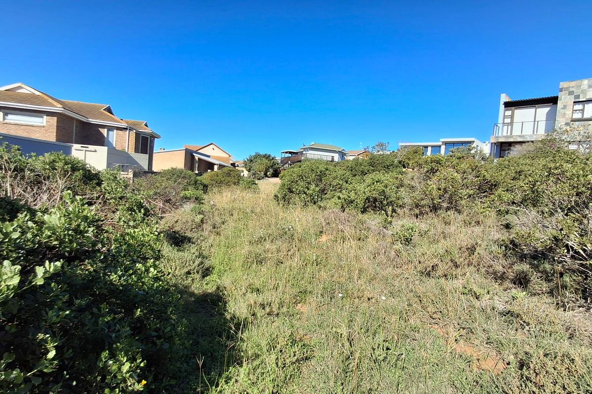 A view of a vacant residential plot featuring natural coastal vegetation and sloped terrain, surrounded by established neighboring properties.