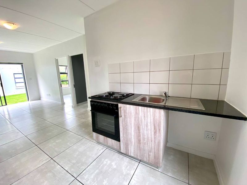 Open-plan living area featuring a compact kitchen with built-in oven, hob, and sink, leading to a bright, tiled living space.