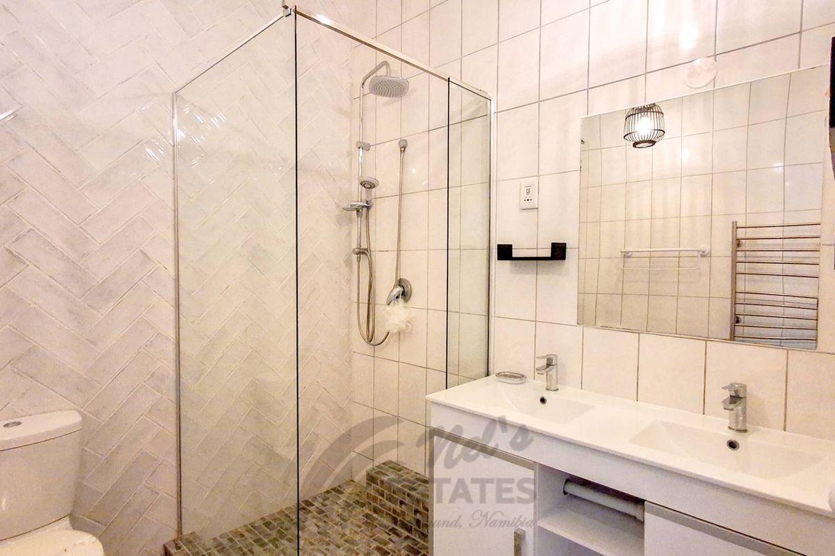 Modern bathroom featuring a glass-enclosed walk-in shower, double vanity with integrated sinks, and stylish herringbone wall tiling.