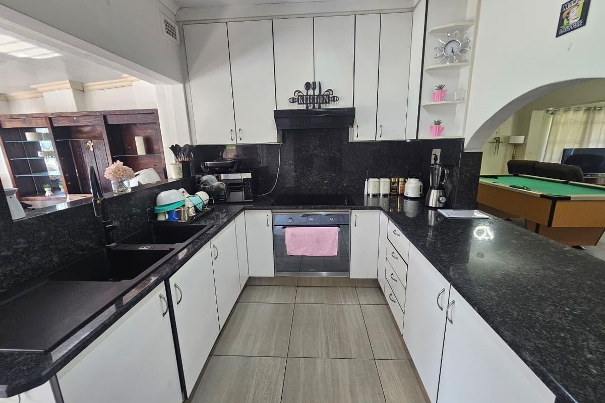 A functional kitchen featuring white cabinetry, dark granite countertops, built-in oven, electric hob, and a double basin sink, opening into the living area.