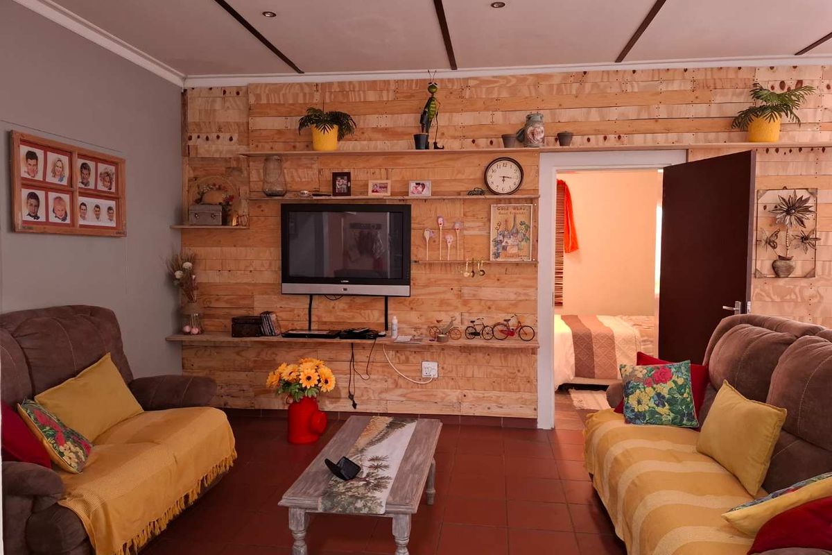 A living room featuring a timber-clad feature wall, tiled flooring, and recessed ceiling beams, providing a rustic aesthetic.