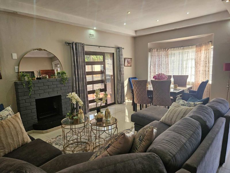 Spacious open-plan living and dining area featuring a brick fireplace, tiled flooring, and natural light through a sliding glass door.