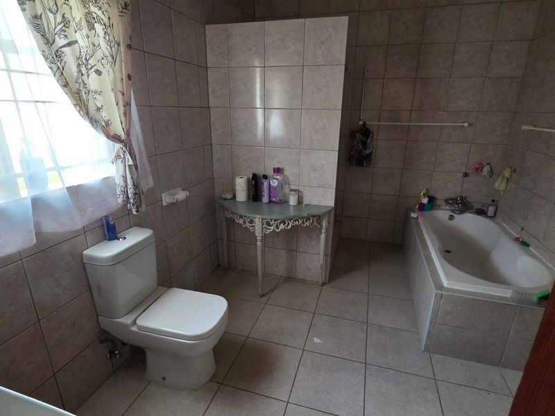 A functional bathroom featuring tiled walls and flooring, a standard toilet, and a built-in bathtub, offering a neutral base for potential cosmetic updates.