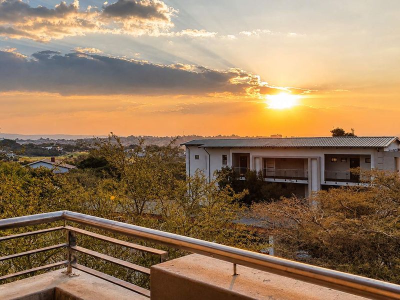 A scenic elevated view overlooking the surrounding landscape and neighboring apartment complex at sunset, featuring a modern stainless steel balcony railing.