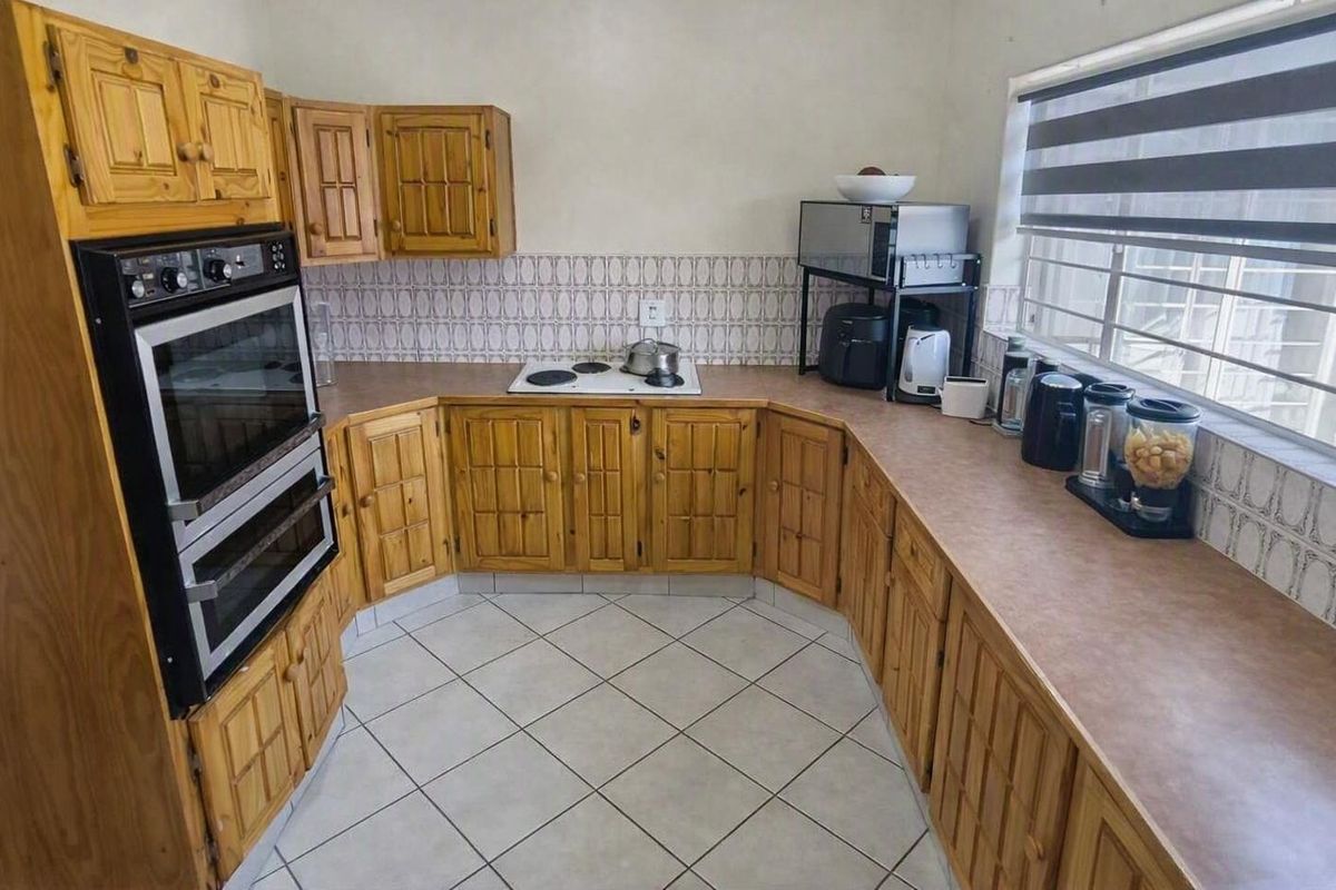 A functional kitchen featuring traditional wooden cabinetry, laminate countertops, a built-in double oven, and an electric hob with tiled backsplash and flooring.