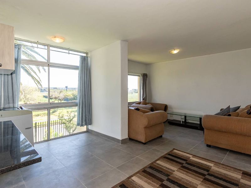 Open-plan living area featuring large windows with natural light, tiled flooring, and a functional kitchen counter space.