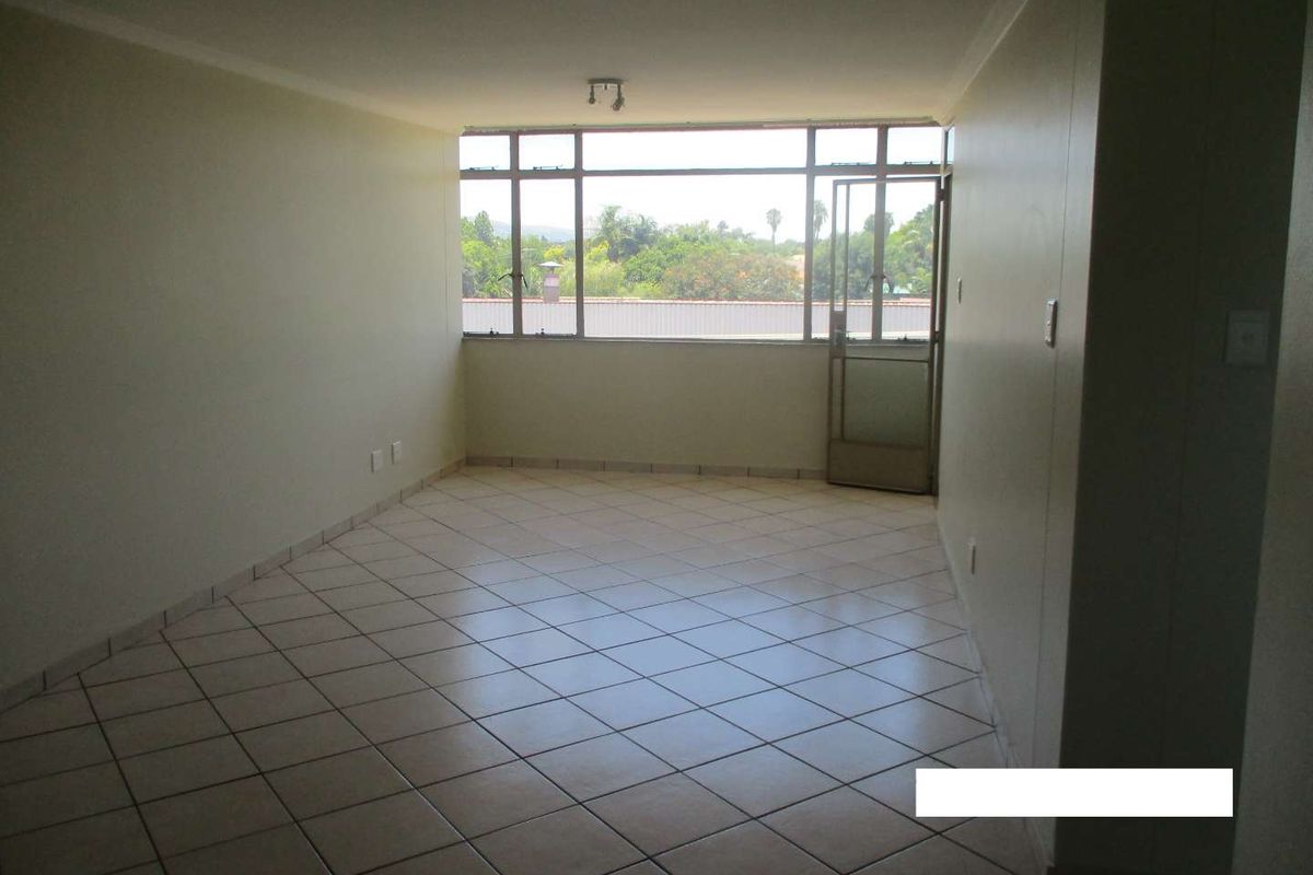 An empty, open-plan living area featuring neutral tiled flooring, large windows providing natural light, and a glass door leading to an outdoor space.
