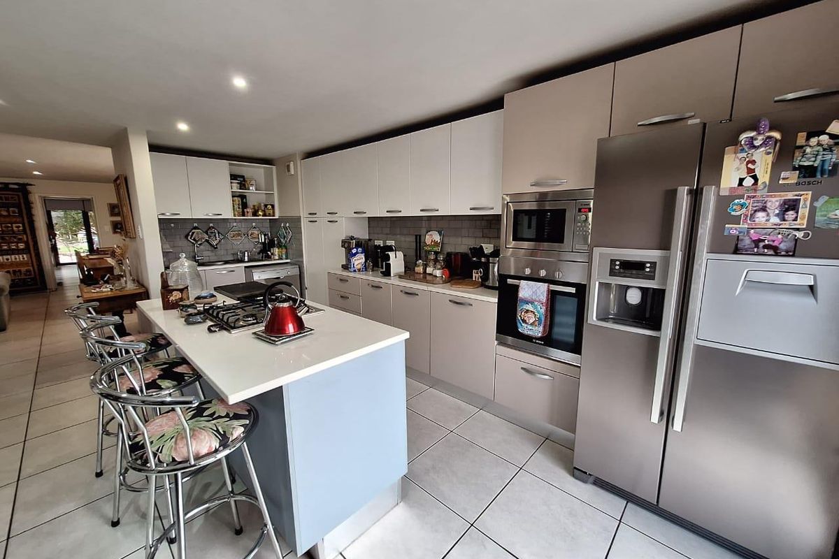 Modern kitchen featuring a central island with gas hob, built-in oven, microwave, and ample cabinetry, finished with light-toned surfaces and tiled flooring.