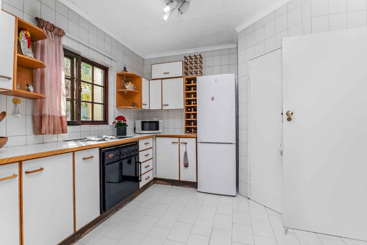 A functional kitchen featuring white cabinetry, tiled walls and flooring, and a built-in oven with hob.