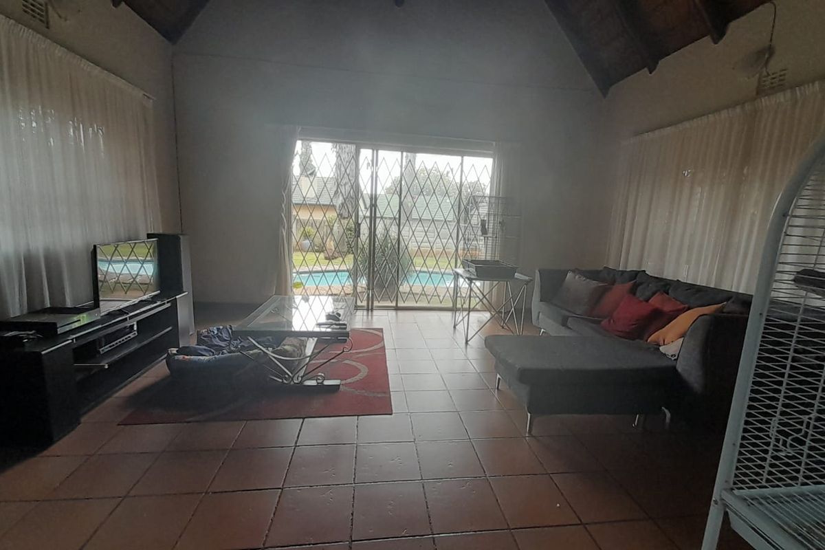 Spacious living room featuring vaulted ceilings, tiled flooring, and large sliding glass doors with security gates providing direct access to the pool area.