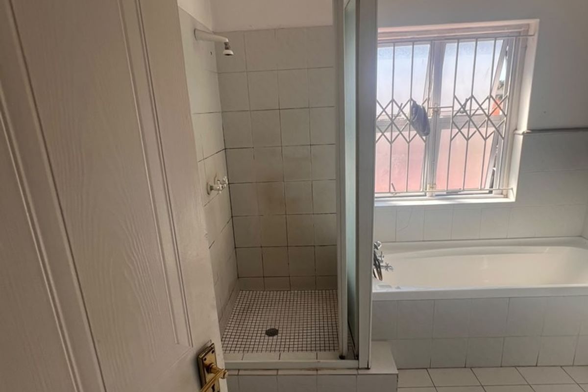 A functional bathroom featuring a built-in bathtub and a separate shower enclosure with tiled finishes and a security-gated window.
