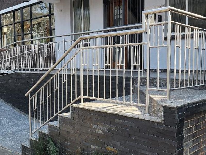 Front entrance of Harrogate apartment building featuring a modern stainless steel railing, stone-clad steps, and an accessible concrete ramp.
