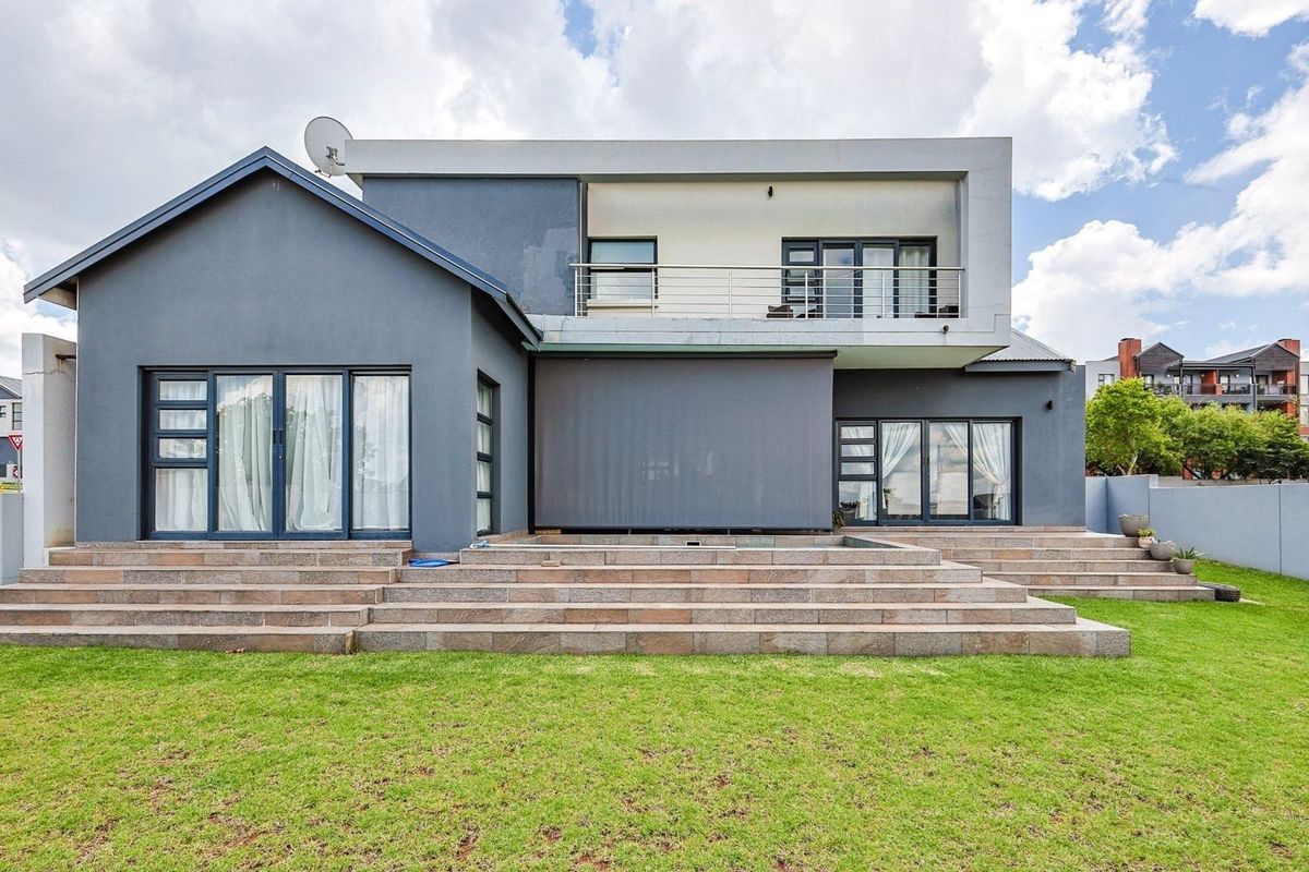 Rear view of a modern two-story house featuring a spacious tiled patio, large glass sliding doors, and a balcony with stainless steel railings.