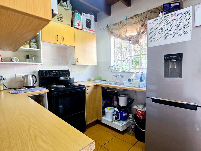 Compact kitchen featuring laminate countertops, built-in cabinetry, a freestanding stove, and a stainless steel sink with a tiled backsplash and exposed timber ceiling beams.