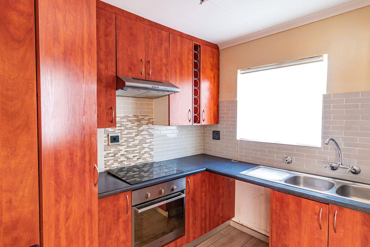 A functional kitchen featuring wood-look laminate cabinetry, built-in oven, electric hob, and a double bowl stainless steel sink with subway tile backsplash.