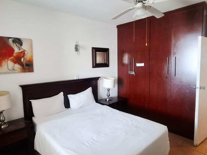 A bedroom featuring built-in wooden wardrobes, a ceiling fan, and tiled flooring, with an adjoining en-suite bathroom.
