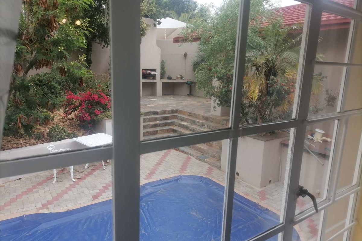 View of a rear garden featuring a paved patio area, built-in braai, and a swimming pool with a cover.