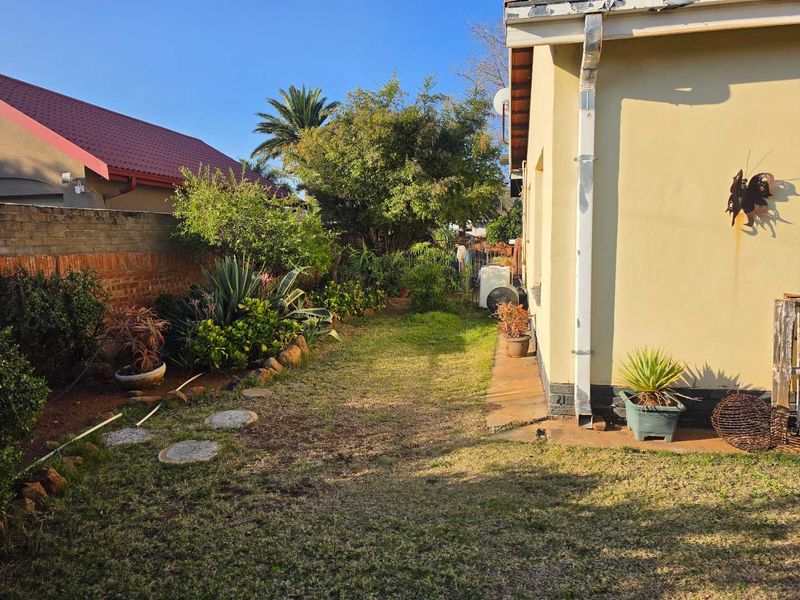 A view of the rear garden featuring a lawn area, established landscaping, and a brick boundary wall along the side of the house.