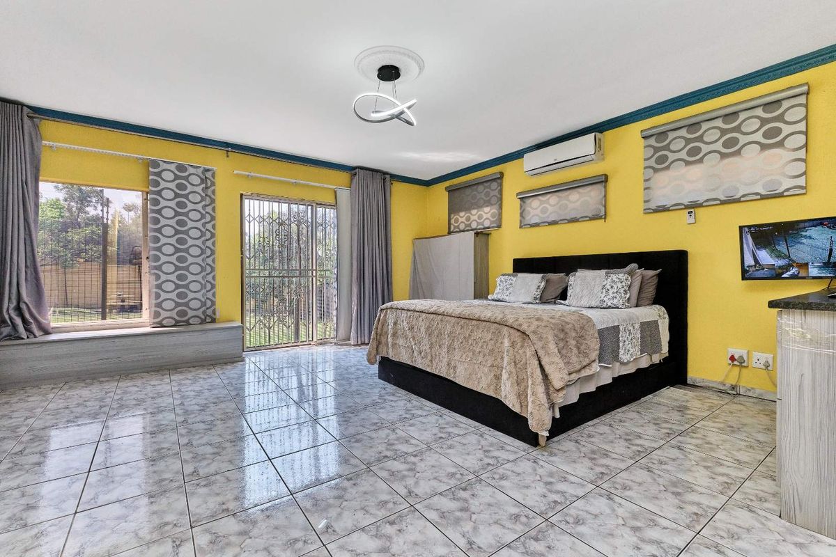 Spacious bedroom featuring tiled flooring, a built-in window seat, and a split-system air conditioner, offering direct access to the exterior through a security gate.